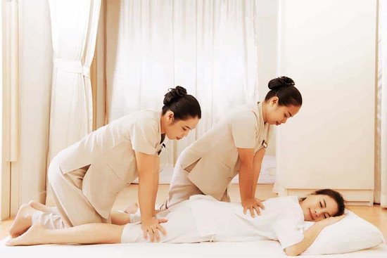 A person lies comfortably on a massage table in a calm, softly lit spa environment while two trained therapists perform a synchronized four hand massage. Both therapists use coordinated, flowing movements with their hands, arms, and elbows to apply balanced pressure across the client’s back, shoulders, and legs. The setting includes clean towels, gentle lighting, and a peaceful atmosphere that promotes relaxation. The client appears at ease, with eyes closed, as the simultaneous motions create a rhythmic and immersive experience designed to release tension and enhance overall well-being. Select 4 more words to run Humanizer.